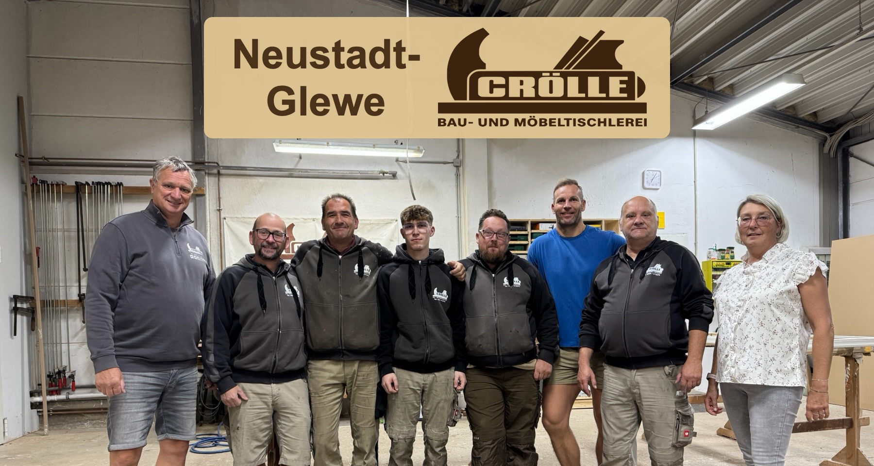 Ein Teil des Teams der Tischlerei Crölle in der Werkstatt in Schwerin; darüber Crölle-Logo und Schriftzug Neustadt-Glewe